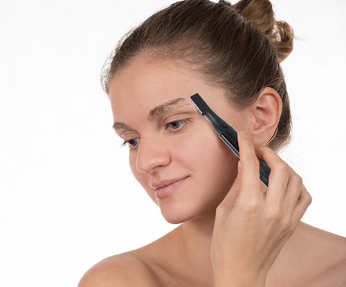 Young girl in a red towel caring for your eyebrows with trimmer